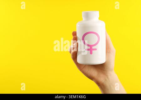Female hormones. Woman holding pill bottle with female gender symbol on yellow background, closeup Stock Photo