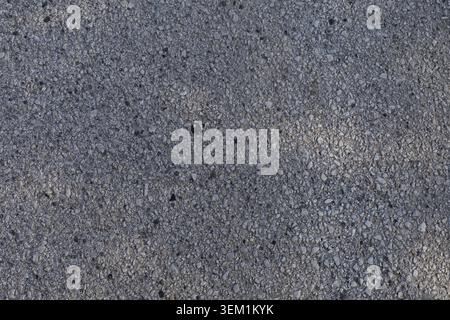 Detailed top view of a rough grey asphalt surface mixed with small stones and fine aggregate gravel particles. Stock Photo