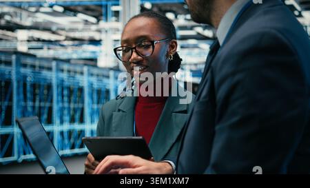 Data center engineering team brainstorming, using AR simulation to monitor systems. Teamworking server hub colleagues collaborating, using devices to do optimizations, VFX overlay, camera A Stock Photo