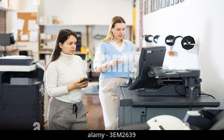 Team of professionals works on printing equipment in printer shop Stock Photo