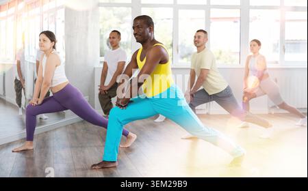 Black male instructor leading stretching for group in dance studio Stock Photo