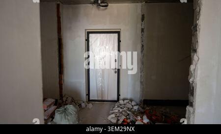 interior view of apartment renovation showing newly installed white door covered in protective plastic film surrounded by plaster debris and exposed b Stock Photo