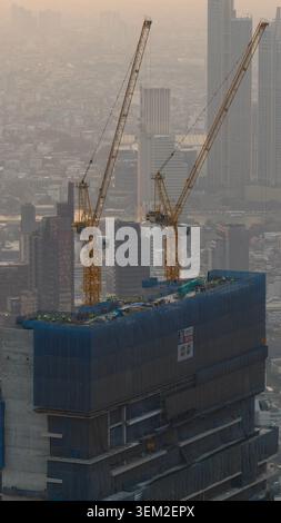 Bangkok, Thailand - 05 February 2026: Aerial view of a skyscraper under construction with two yellow tower cranes and workers on the roof against a ha Stock Photo