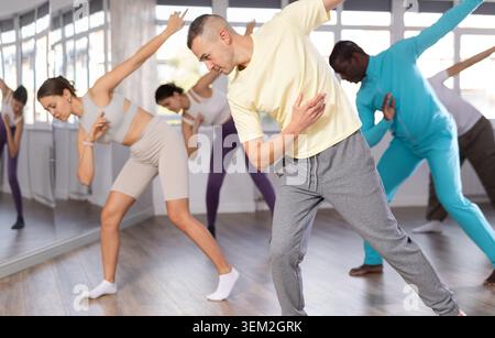 Happy young man and multinational group of active people in sportswear dancing rock and roll dance in dance studio during Stock Photo