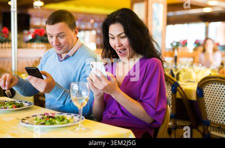 Adult biracial using phones during lunch in restaurant Stock Photo