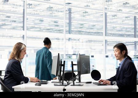 Using AI machine learning, computer monitor and multiracial team designing complex PCB layout. Optimizing integrated circuit production, artificial intelligence and teamworking colleagues Stock Photo