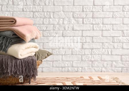 Wicker basket with cozy blankets near white brick wall Stock Photo