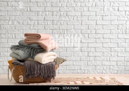 Wicker basket with cozy blankets near white brick wall Stock Photo