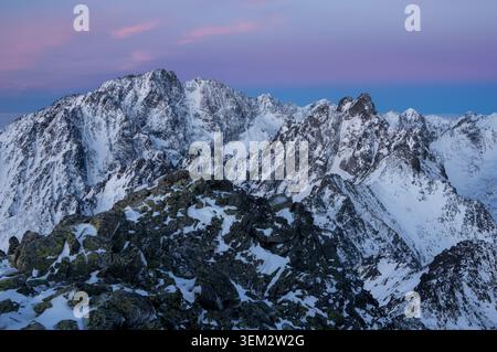 View of Slavkovsky stit and the snow-covered peaks of the High Tatras mountains under a purple twilight sky Vysoke Tatry, Presovsky kraj, Slovakia. Stock Photo