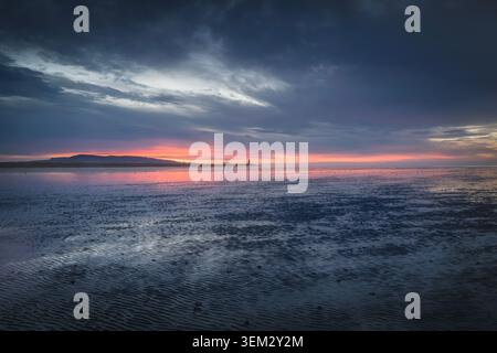 View of the sunset over the sea with the South Wall lighthouse in the distance under a dramatic cloudy sky County Dublin, Ireland. Stock Photo