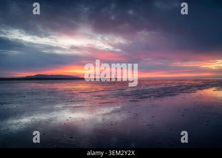 View of the South Wall and Poolbeg Lighthouse at sunrise with vibrant pink and orange reflections on the wet sand of the bay in County Dublin, Ireland Stock Photo
