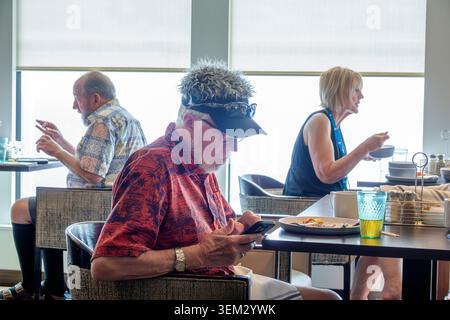 Caribbean Sea,senior man,mature adult,older male,mobile phone smartphone,texting,checking messages,seated passenger,senior woman,mature female,eating Stock Photo