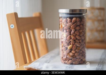 A clear jar holds peanuts on a wooden table by a chair Stock Photo