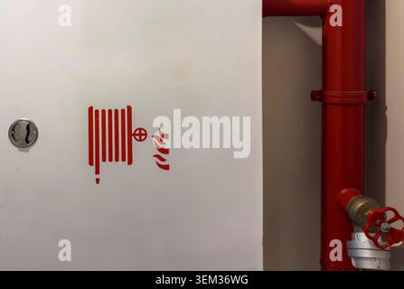 View of a white fire hose cabinet with a red reel icon next to a red fire protection pipe and valve in Avcilar, Istanbul, Turkiye. Stock Photo