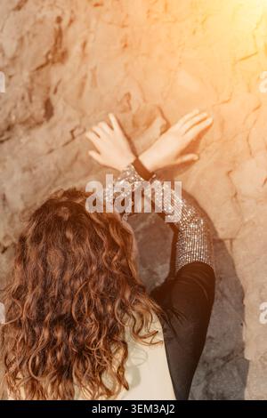 Woman hair rock leaning against a textured stone wall during golden hour with warm sunlight and copy space Stock Photo