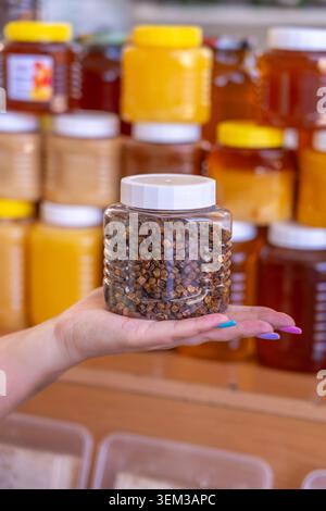 Close-up. A jar of bee bread in a palm, against a background of jars of various types of honey. Concept: bees give us health Stock Photo