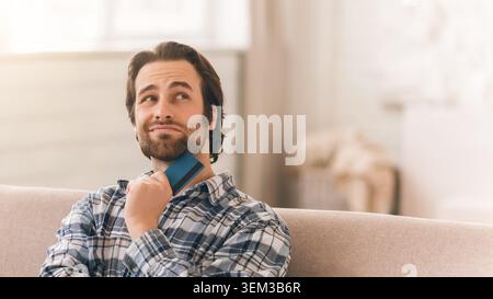 Thoughtful Caucasian Man Holding Credit Card, Considering Online Shopping At Home, Business Concept Stock Photo