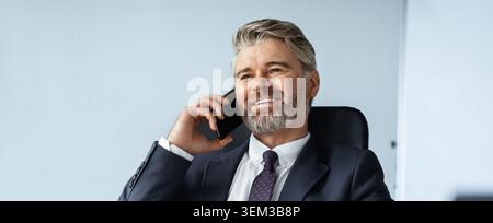 Smiling Caucasian Businessman Talking On Phone In Modern Office, Business Concept Stock Photo