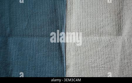 Two pieces of textured cloth are arranged side by side on a flat surface. One cloth is dark blue, and the other is light gray, showing their unique pa Stock Photo