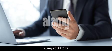 Businessman Holding Smartphone While Working On Laptop In Modern Office, Professional Concept Stock Photo