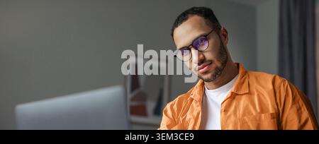 Focused Young Man Working On Laptop At Home Office, Professional Setting Stock Photo