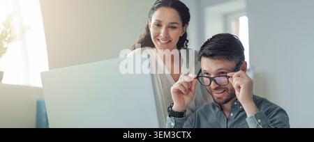 Happy Woman Smiling At Man Adjusting Glasses In Modern Office, Business Concept Stock Photo