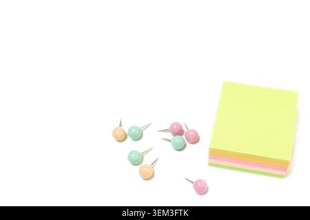 Top view horizontal closeup of colorful sticky note pad stack with pastel push pins scattered nearby on white copy space background Stock Photo