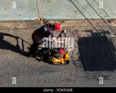 Marilia, SP, Brazil, June 03, 2026: A construction worker in uniform operates a yellow vibratory plate compactor machine during road maintenance and a Stock Photo