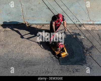 Marilia, SP, Brazil, June 03, 2026: A construction worker in uniform operates a yellow vibratory plate compactor machine during road maintenance and a Stock Photo