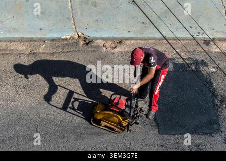 Marilia, SP, Brazil, June 03, 2026: A construction worker in uniform operates a yellow vibratory plate compactor machine during road maintenance and a Stock Photo