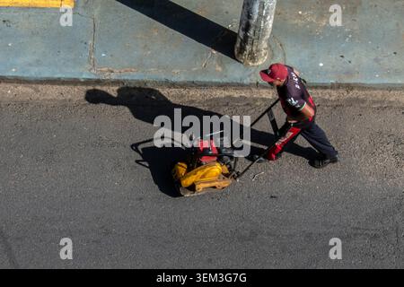 Marilia, SP, Brazil, June 03, 2026: A construction worker in uniform operates a yellow vibratory plate compactor machine during road maintenance and a Stock Photo