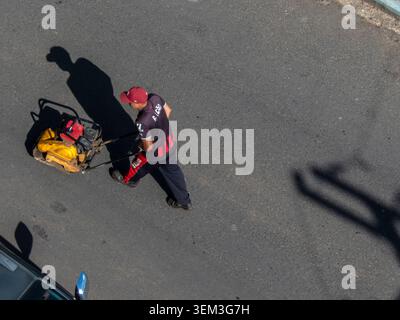 Marilia, SP, Brazil, June 03, 2026: A construction worker in uniform operates a yellow vibratory plate compactor machine during road maintenance and a Stock Photo