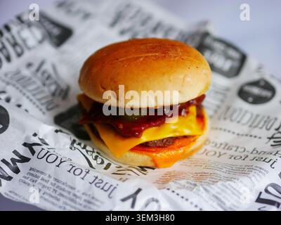 A cheeseburger on a piece of printed paper features a toasted bun, melted cheddar cheese, beef patty, beef bacon, an onion ring, and barbecue sauce. Stock Photo