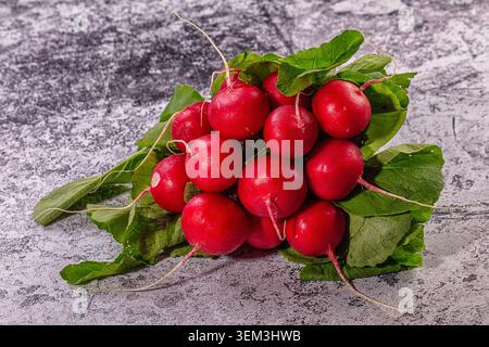 Vibrant red radishes with fresh green leaves arranged on textured grey surface. Bright natural light illuminates crisp vegetables, emphasizing healthy Stock Photo