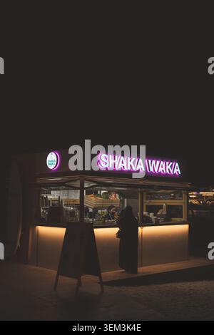 Neon lit food kiosk at night with a person standing at the counter and warm lights glowing in the dark street Stock Photo