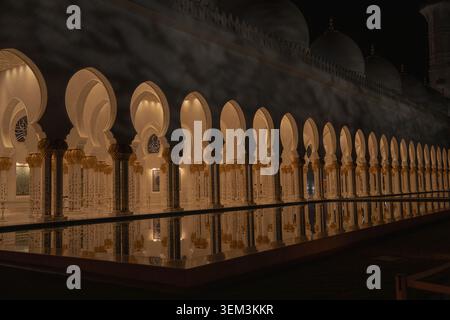 Night view of a long arched colonnade with warm lights reflecting in still water, creating a calm and elegant architectural scene Stock Photo
