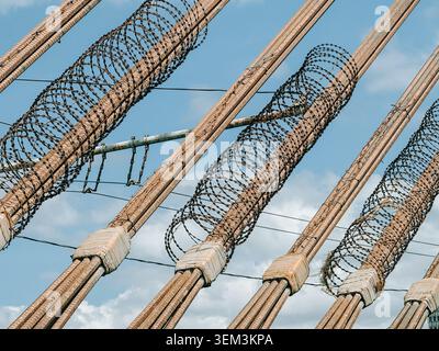 Riga, Latvia - June 4, 2026: Close-up view of coiled barbed wire wrapped around structural steel elements against a blue sky. Strong visual for securi Stock Photo
