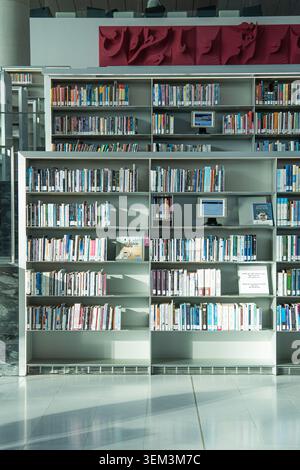 Rows of books on tall shelves in a modern library interior with computer stations and a bright empty floor Stock Photo