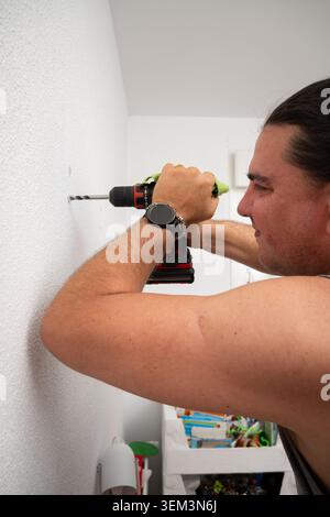 Man drilling into a white wall using an electric power tool for home renovation Stock Photo