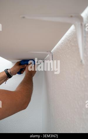 Man installing a new shelf with brackets and an electric screwdriver Stock Photo