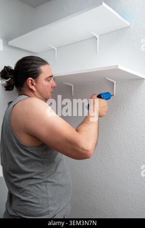 Man using power tool to mount storage shelves on a wall for DIY project Stock Photo
