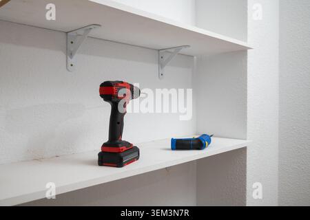 Cordless drill and screwdriver resting on white shelf, ready for home improvement Stock Photo