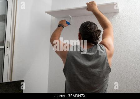 Man installing a new shelf with brackets on a white wall Stock Photo