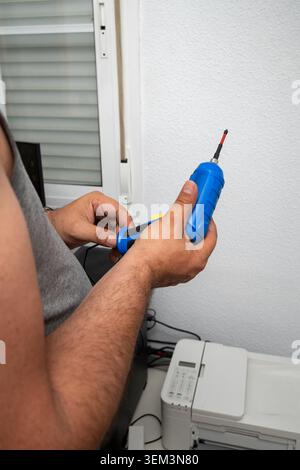 Man's hands holding an electric screwdriver, repairing a printer in an office setting Stock Photo