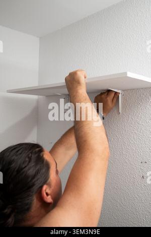 Man installing a new shelf with brackets on a white textured wall in a home Stock Photo