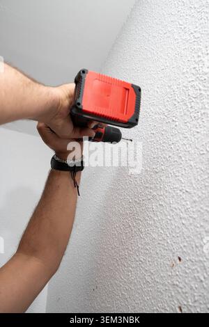 Person's hands using a cordless power drill to make a new hole in a white wall Stock Photo