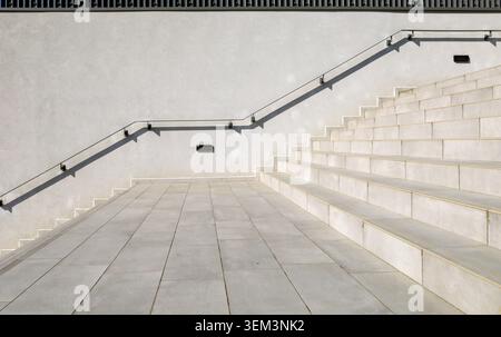 Handrails on the side of gray plaster wall along the large stone tiled staircase. Background for copy space. Stock Photo