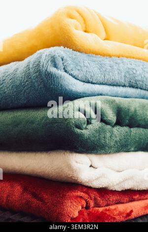 Colorful blankets stacked on  shelf in  bright room during daytime. Several blankets of different colors are neatly stacked on a shelf. soft texture o Stock Photo