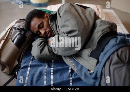 Black Adult Man Resting in Humanitarian Aid Shelter Bed Stock Photo