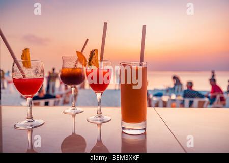 Refreshing tropical cocktail drinks on beach bar table at golden sunset by sea. Summer holiday party paradise. Cocktail beach vacation travel resort Stock Photo